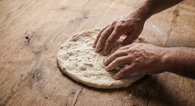 mani ricoperte di farina che stendono l'impasto della pizza